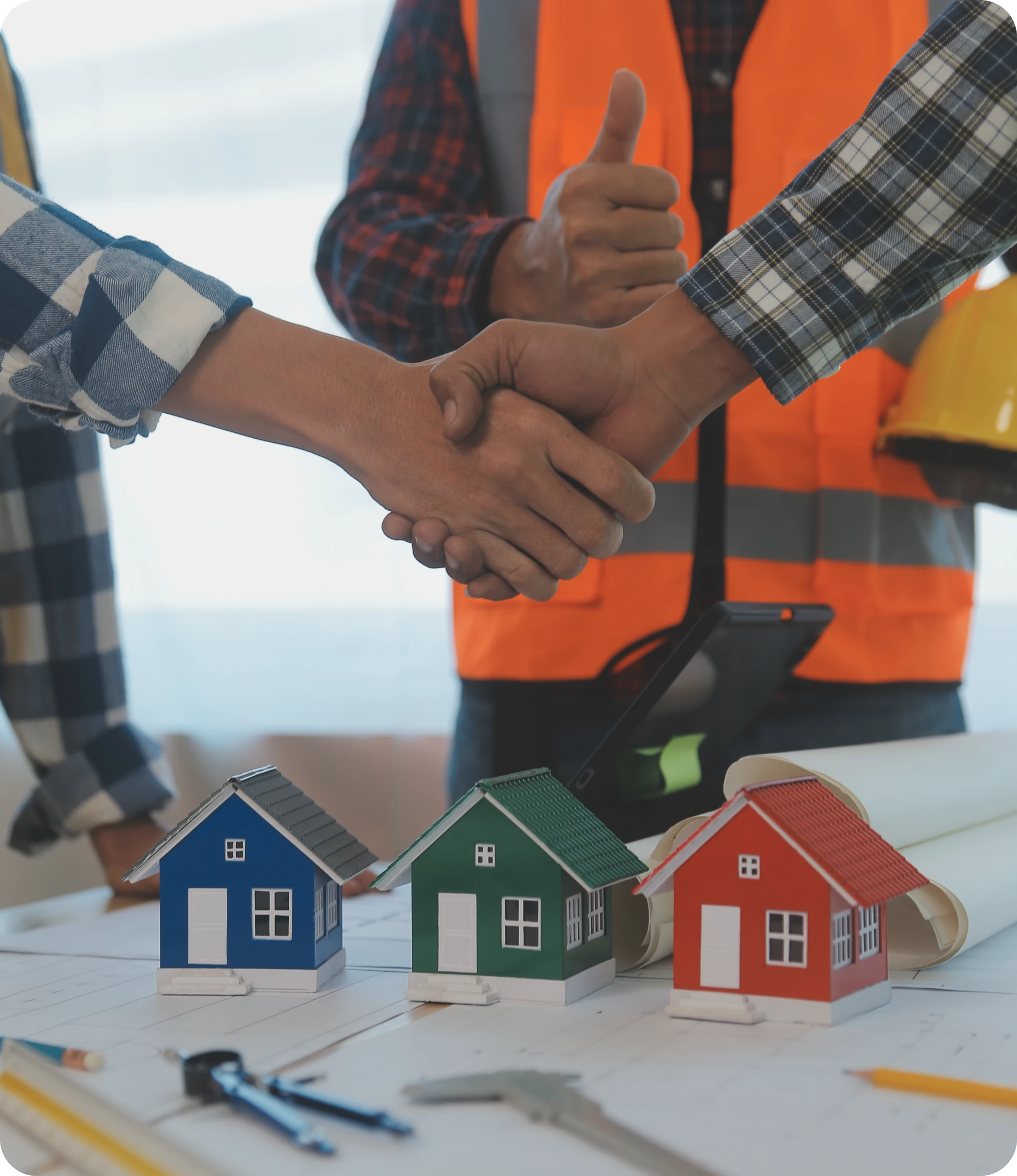 Handshake Over Table With Model Houses, Blueprints & Orange Safety Vest