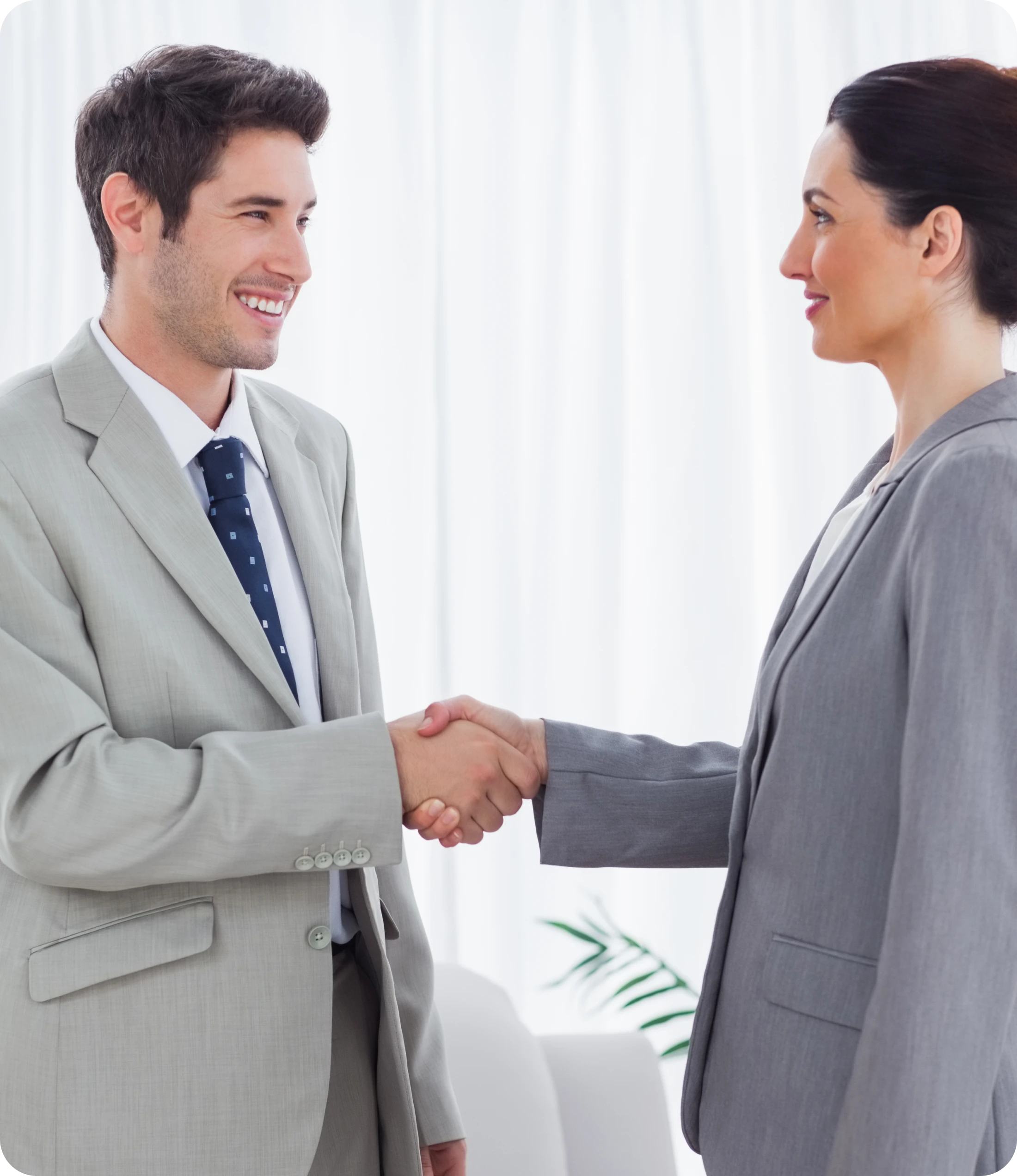 Man In Grey Suit & Dark Tie Shaking Hands With Woman In Grey Blazer